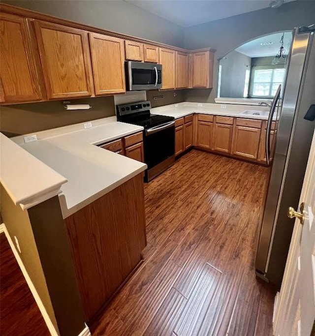 kitchen with a peninsula, appliances with stainless steel finishes, dark wood-type flooring, and light countertops