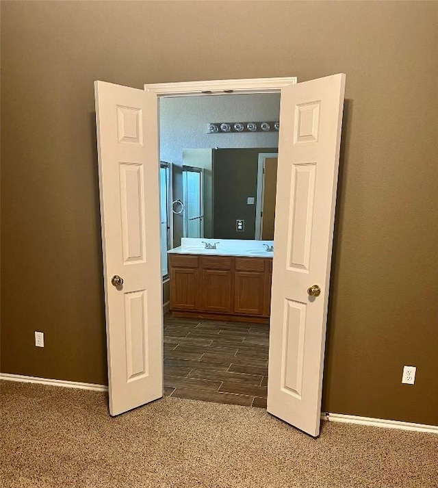 corridor with dark carpet, baseboards, and a sink