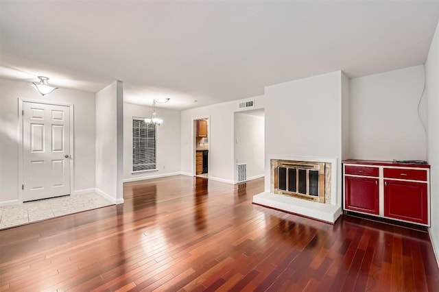 unfurnished living room with an inviting chandelier, a glass covered fireplace, wood finished floors, and visible vents