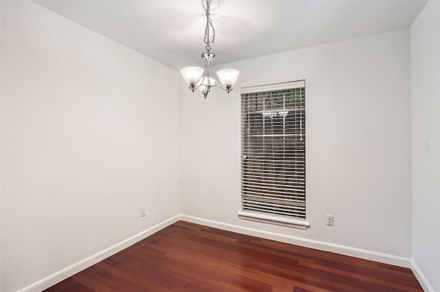 spare room featuring baseboards, dark wood-style flooring, and a chandelier