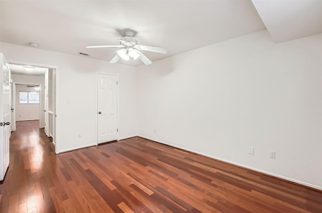empty room featuring dark wood-style floors, baseboards, a ceiling fan, and visible vents