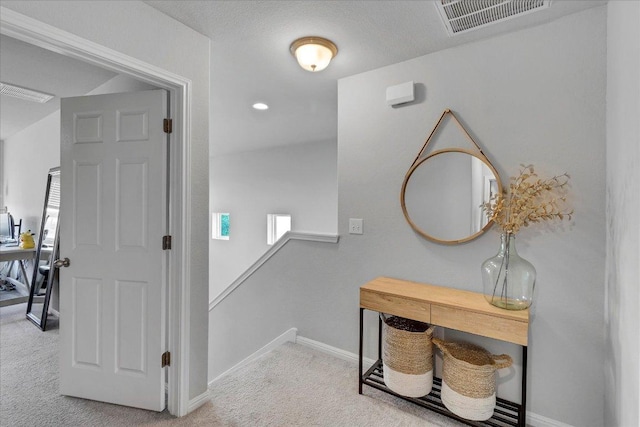 hall featuring baseboards, visible vents, an upstairs landing, and carpet flooring