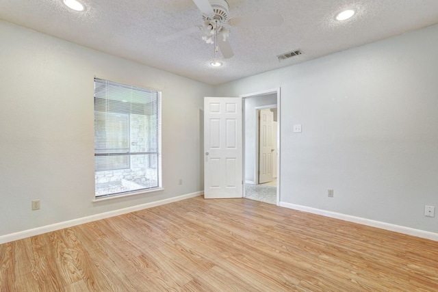 empty room featuring ceiling fan, light wood finished floors, a textured ceiling, and visible vents