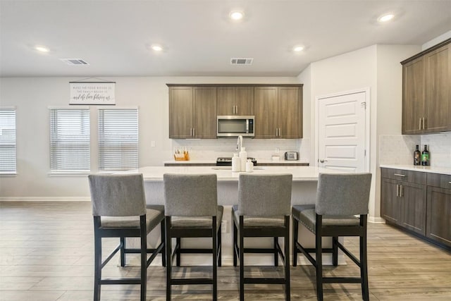 10310 Mager Ln, Hutto, TX 78634 - kitchen featuring stainless steel microwave, an island with sink, backsplash, light countertops, and a kitchen bar