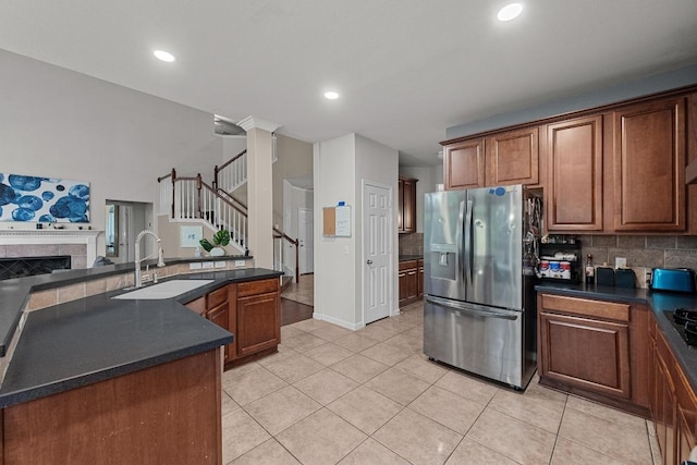 kitchen featuring stainless steel fridge with ice dispenser, dark countertops, a sink, and a fireplace