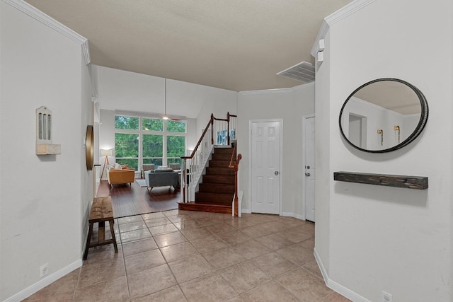 entrance foyer with stairway, light tile patterned floors, baseboards, ornamental molding, and visible vents