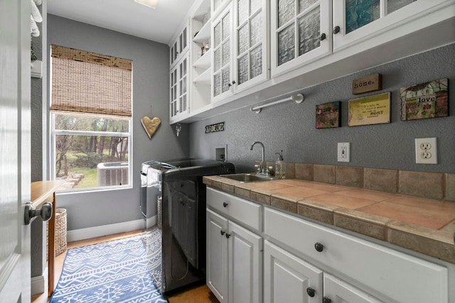 laundry room featuring light wood finished floors, washer and clothes dryer, a sink, baseboards, and cabinet space