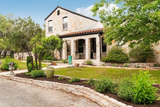mediterranean / spanish home with stone siding, a tile roof, a front lawn, and covered porch