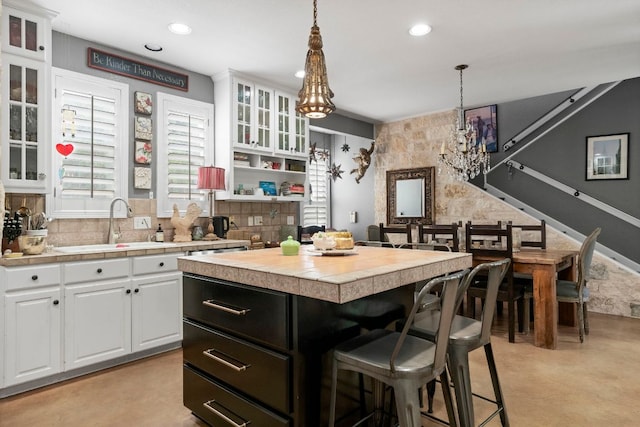 kitchen featuring white cabinets, a sink, a chandelier, pendant lighting, and a breakfast bar area