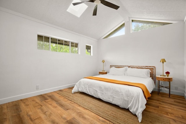 bedroom with wood finished floors, baseboards, a ceiling fan, and vaulted ceiling with skylight