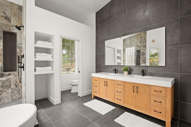 bathroom with a tile shower, toilet, a sink, and double vanity