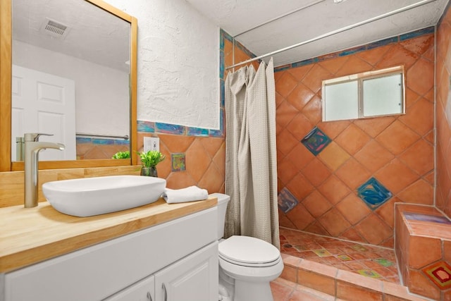full bath with vanity, tile walls, a tile shower, toilet, and visible vents