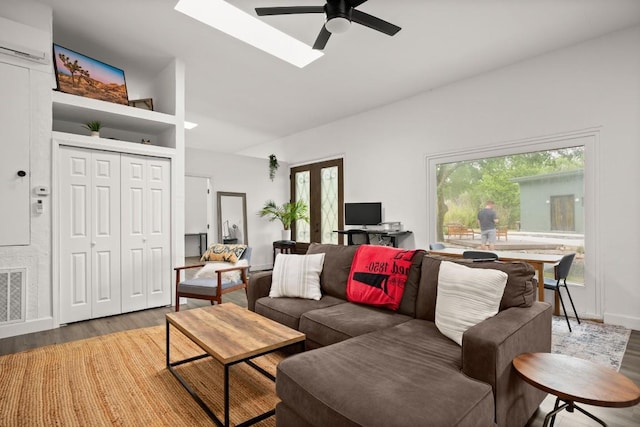 living room featuring visible vents, an AC wall unit, a ceiling fan, a skylight, and light wood-style flooring