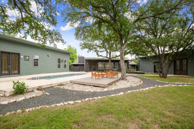 rear view of property with an outdoor pool, a deck, french doors, a yard, and stucco siding