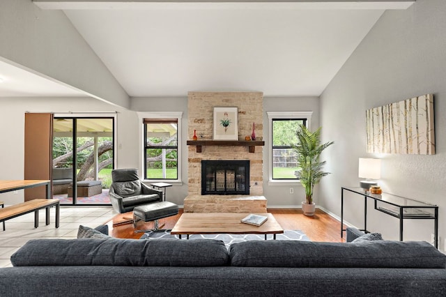 living area with baseboards, wood finished floors, a stone fireplace, and high vaulted ceiling