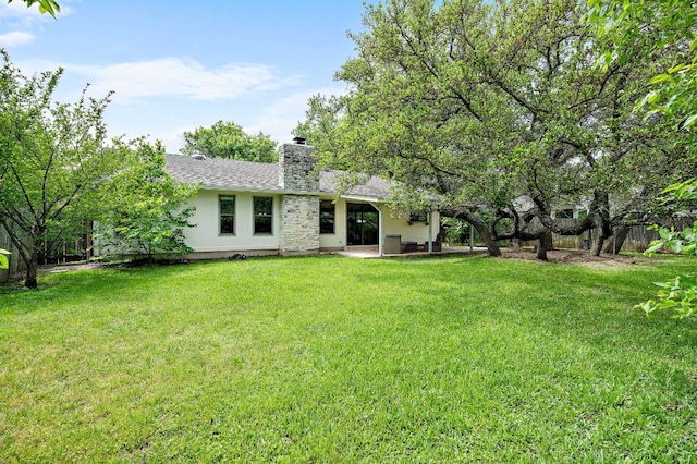 rear view of property with roof with shingles, a chimney, fence, a patio area, and a lawn