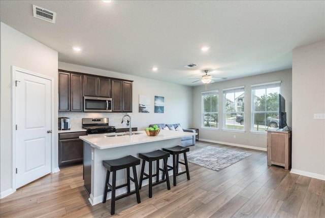 943 Lone Peak Way, Dripping Springs, TX 78620 - kitchen featuring appliances with stainless steel finishes, a sink, open floor plan, light wood-type flooring, and dark brown cabinetry