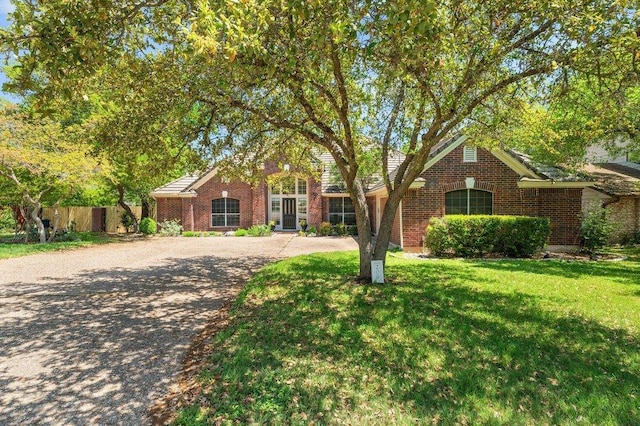 view of front of property with brick siding, driveway, a front lawn, and fence
