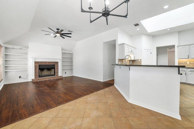 kitchen with lofted ceiling with skylight, dark countertops, visible vents, built in features, and a ceiling fan