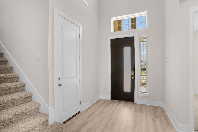 foyer featuring baseboards, light wood finished floors, and stairs
