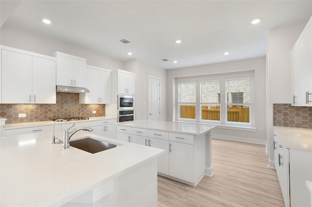kitchen with stainless steel appliances, a sink, visible vents, under cabinet range hood, and a kitchen island