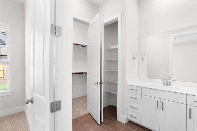 bathroom featuring baseboards, vanity, tile patterned flooring, and a walk in closet