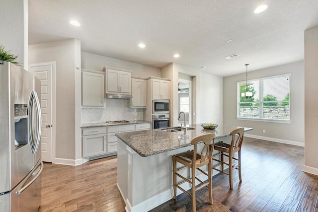 4228 Hannover Way, Round Rock, TX 78681 - kitchen with appliances with stainless steel finishes, wood finished floors, backsplash, light stone countertops, and a breakfast bar area