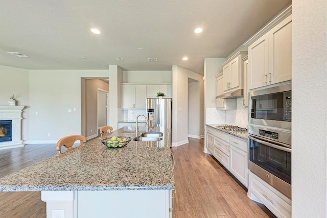 4228 Hannover Way, Round Rock, TX 78681 - kitchen with appliances with stainless steel finishes, under cabinet range hood, decorative backsplash, a center island with sink, and recessed lighting