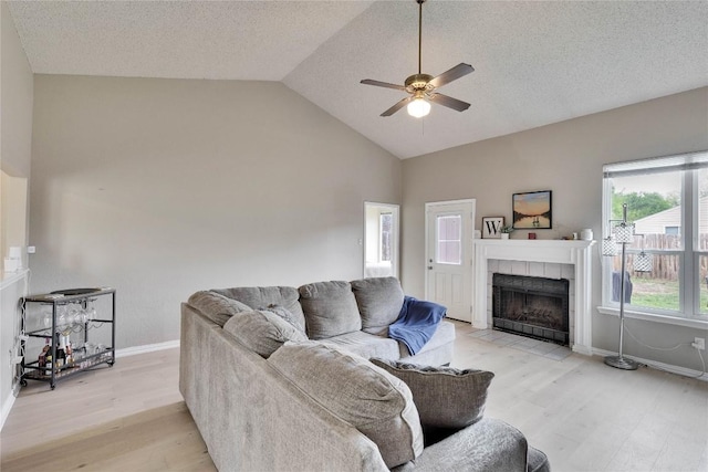 3100 Jubilee Trl, Austin, TX 78748 - living room with light wood-style flooring, a ceiling fan, a tiled fireplace, baseboards, and a textured ceiling