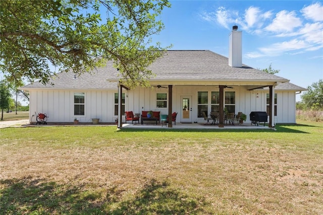back of property with board and batten siding, ceiling fan, a lawn, and a chimney