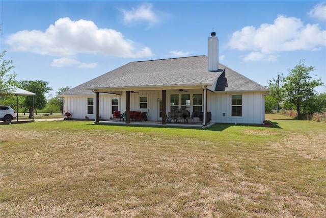 back of property with a ceiling fan, a chimney, board and batten siding, a patio area, and a lawn