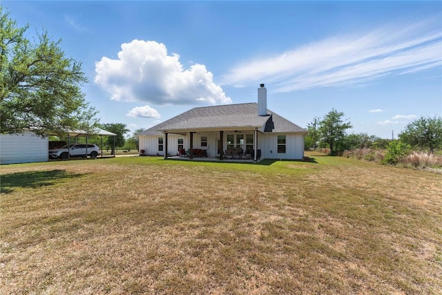 back of property featuring board and batten siding, a lawn, a chimney, and a detached carport