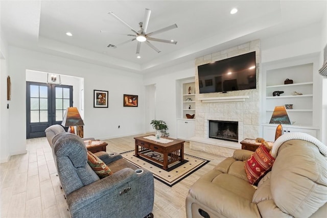 living room with built in shelves, ceiling fan, french doors, a tray ceiling, and baseboards
