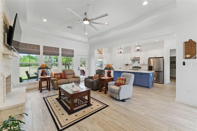 living area featuring a tray ceiling, light wood finished floors, a ceiling fan, and recessed lighting