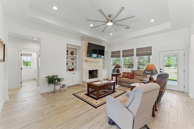 living room with recessed lighting, a raised ceiling, a stone fireplace, light wood-style flooring, and ceiling fan