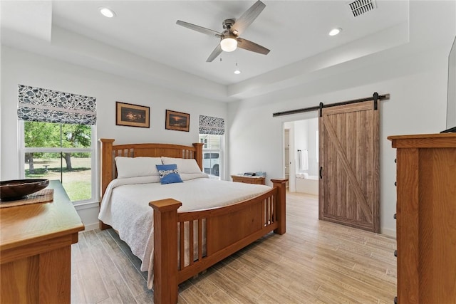 bedroom featuring a barn door, light wood-type flooring, visible vents, recessed lighting, and a raised ceiling