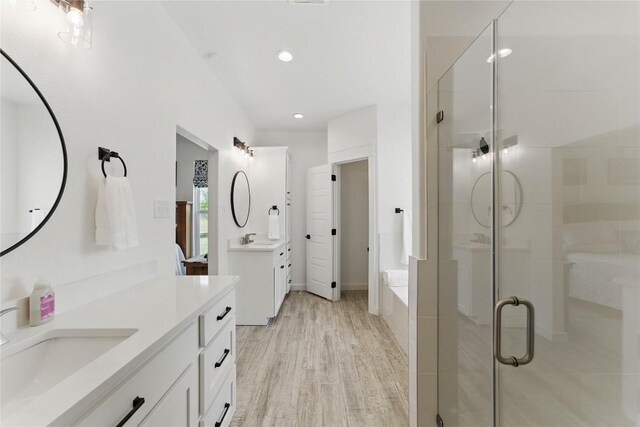 full bathroom featuring two vanities, wood finished floors, a sink, and a stall shower