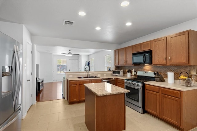 6801 Campina Xing, Del Valle, TX 78617 - kitchen with stainless steel appliances, a peninsula, decorative backsplash, brown cabinetry, and recessed lighting