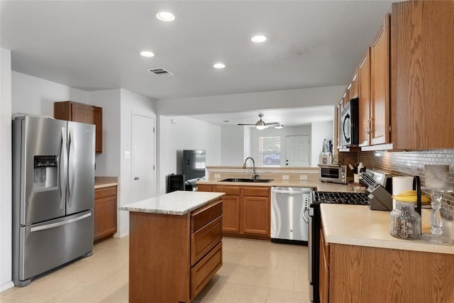 6801 Campina Xing, Del Valle, TX 78617 - kitchen featuring appliances with stainless steel finishes, light countertops, a peninsula, brown cabinetry, and a ceiling fan