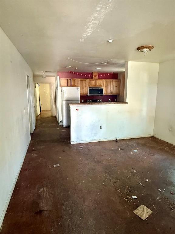 7307 Thannas Way, Austin, TX 78744 - kitchen with stainless steel microwave, freestanding refrigerator, unfinished concrete flooring, a peninsula, and brown cabinets