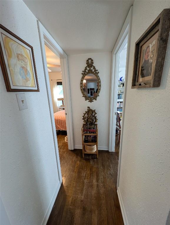 corridor featuring baseboards, a textured wall, and dark wood-type flooring