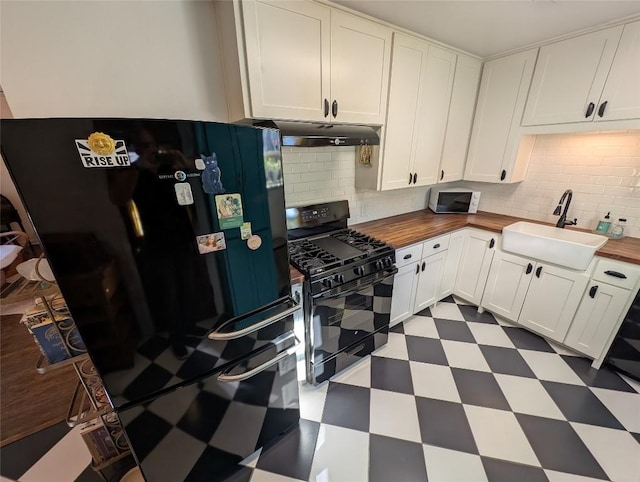 kitchen featuring a sink, wood counters, dark floors, under cabinet range hood, and black appliances