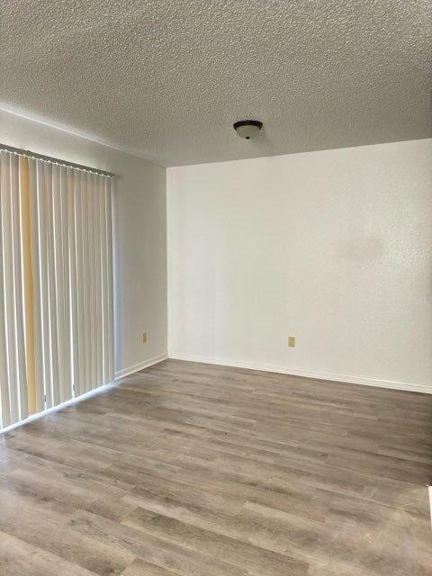 spare room with baseboards, wood finished floors, and a textured ceiling