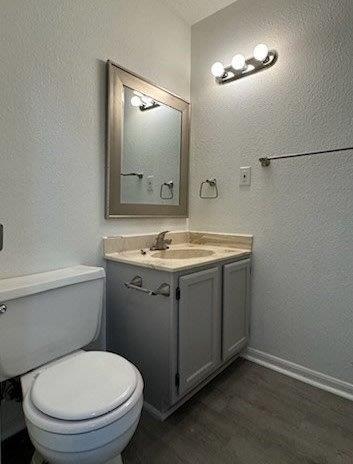 half bathroom with baseboards, wood finished floors, toilet, and vanity
