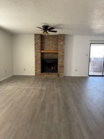 unfurnished living room with wood finished floors, a textured ceiling, ceiling fan, baseboards, and a brick fireplace