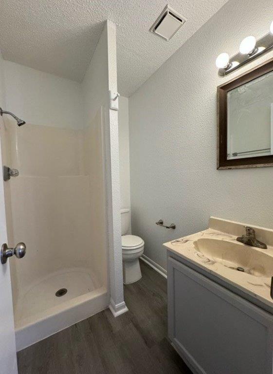 full bath featuring a shower stall, wood finished floors, vanity, toilet, and visible vents
