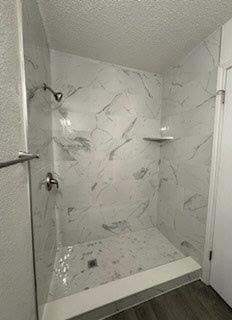 bathroom with wood finished floors, a textured ceiling, and a marble finish shower