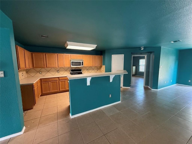 kitchen featuring stainless steel microwave, light countertops, decorative backsplash, and light tile patterned floors