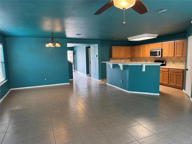 kitchen with stainless steel microwave, backsplash, tile patterned flooring, and a kitchen breakfast bar