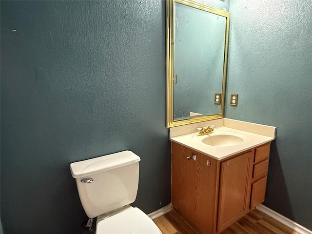 bathroom with toilet, vanity, wood finished floors, and baseboards